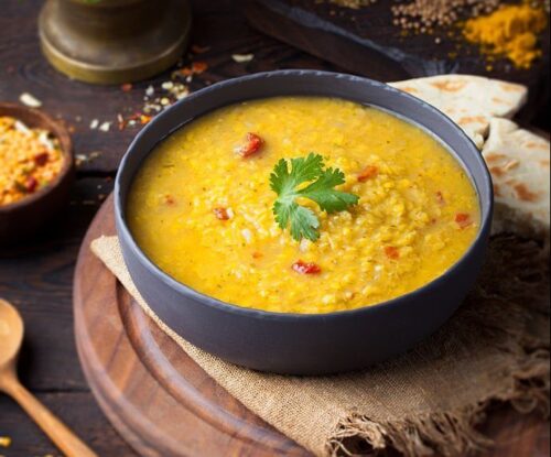 Red lentil Indian soup with flat bread on a wooden background. Masoor dal. KERALI RESTAURANT & BAR