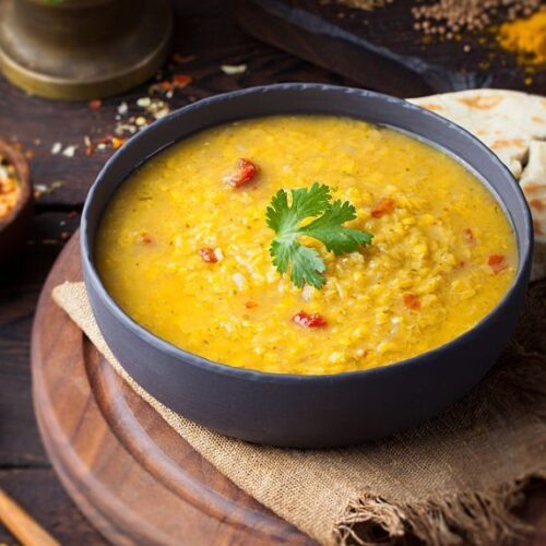 Red lentil Indian soup with flat bread on a wooden background. Masoor dal. KERALI RESTAURANT & BAR